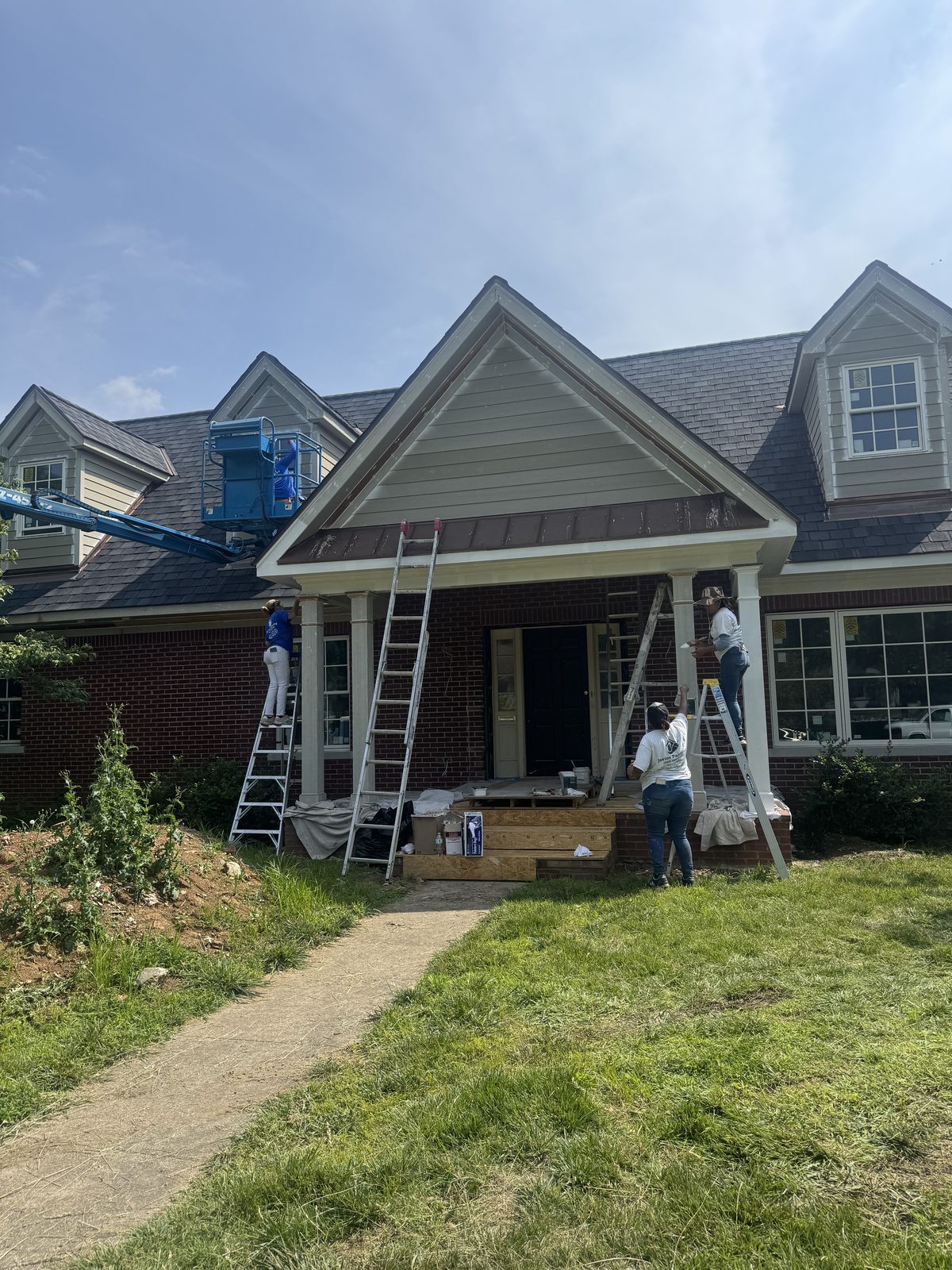 Javier Painting crew on ladders and a lift painting a large home exterior gable